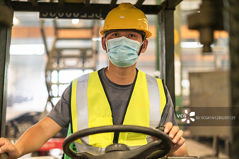 一名戴着面罩的男性工人正在驾驶叉车图片素材