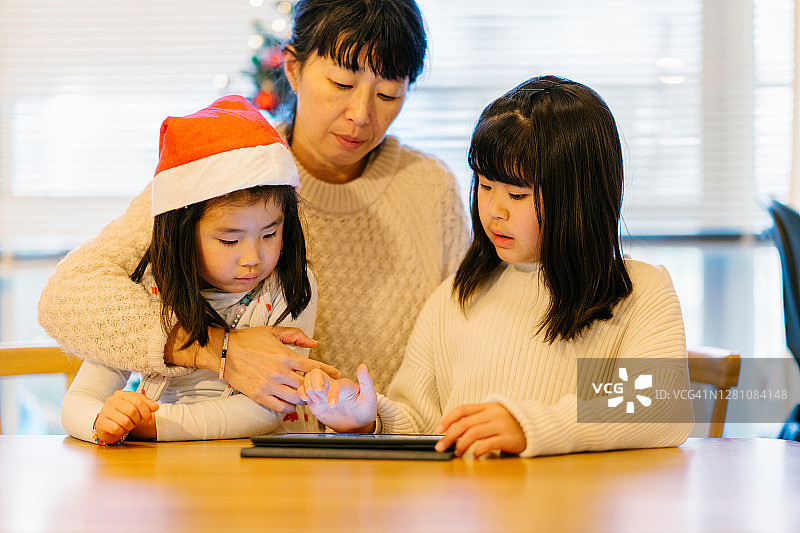 母亲带着两个年幼的孩子使用平板电脑与其他家庭成员远程联系图片素材