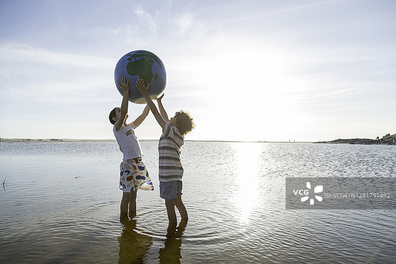 两个孩子在一个泻湖里举起一个大地球仪图片素材