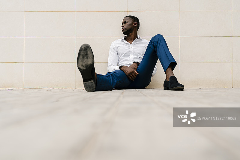 疲惫的非洲企业家在人行道上靠墙坐着休息的时候看向别处图片素材