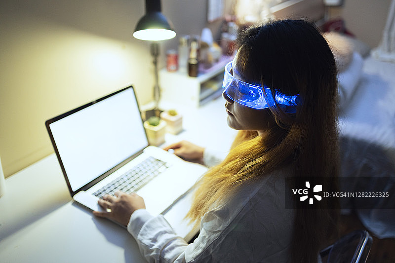 戴着增强现实眼镜在家用笔记本电脑的女人图片素材