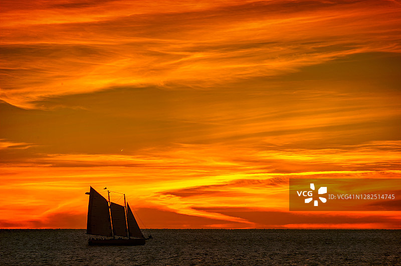 在佛罗里达基韦斯特的日落下，三帆纵帆船在壮观的天空下航行图片素材