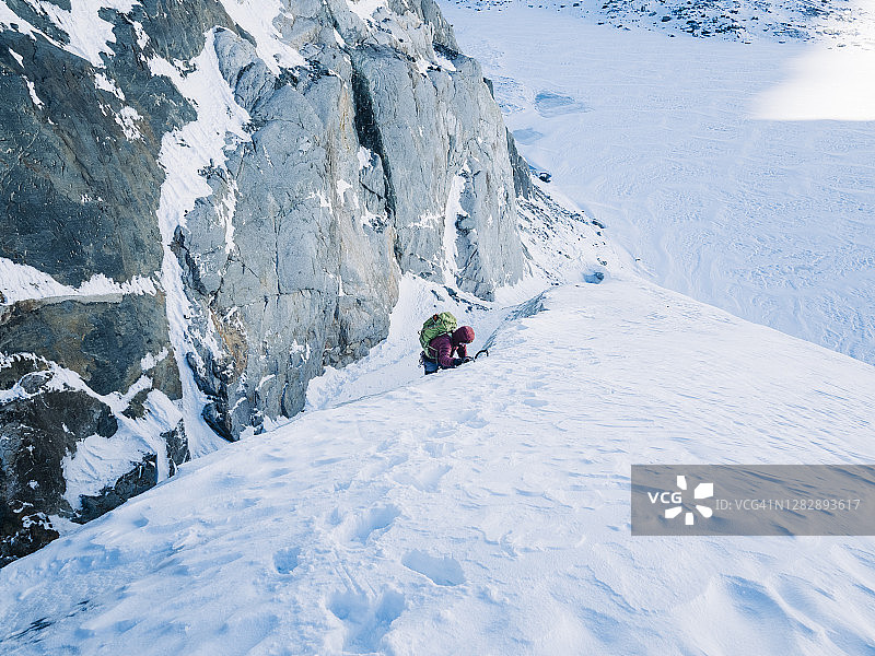 一个冰上攀登者手拿两把冰斧爬上冰川上陡峭的雪坡图片素材