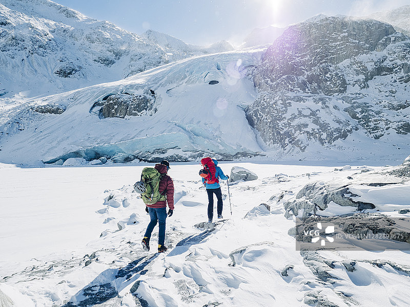 在一个寒冷多风的日子里，两名登山者在雪地上走着，空中飘着鹅毛大雪图片素材