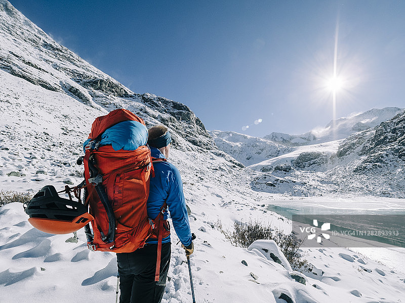 在一个阳光明媚的日子里，一个背着背包的登山者在白雪覆盖的风景中眺望远处的一座山图片素材