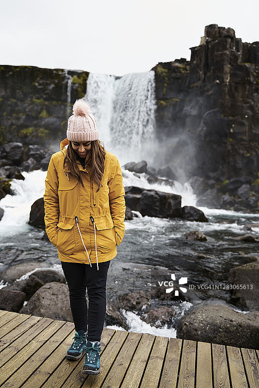 积极的年轻女子放松附近风景如画的瀑布在岩石峡谷图片素材