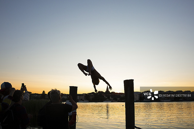 当朋友们在日落时分在湖边拍照时，一个男人向后翻转图片素材