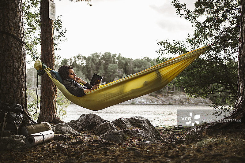 一个年轻人躺在森林里的吊床上看书图片素材