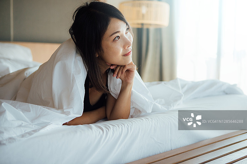 微笑美丽的年轻女人在床上做白日梦图片素材