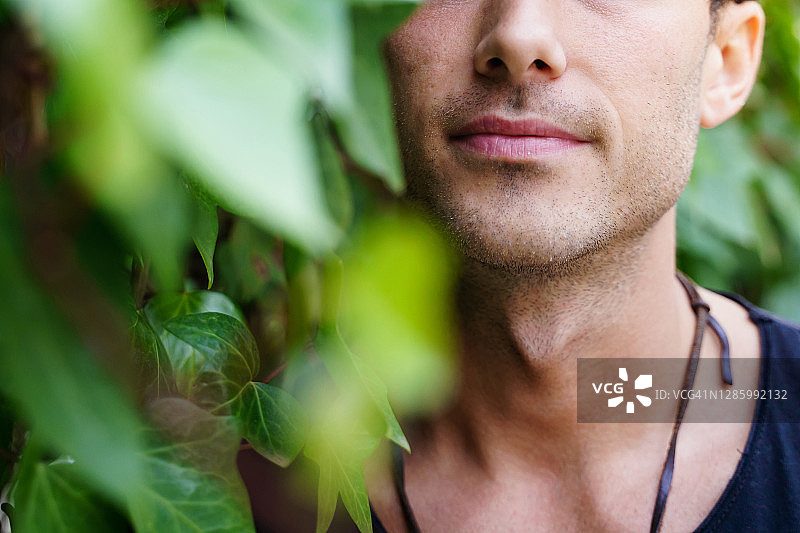 细节的嘴和颈部坚果的一个年轻人旁边的攀缘植物与放松的表情户外图片素材