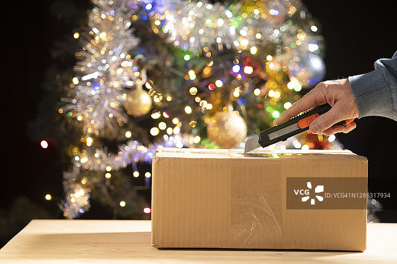 在圣诞树前打开包裹的人。图片素材
