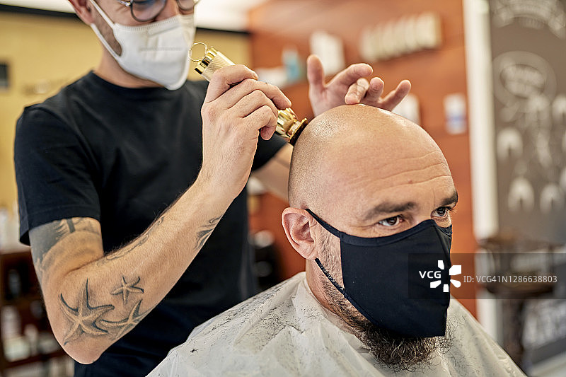 COVID-19期间理发师为男性客户剃须图片素材