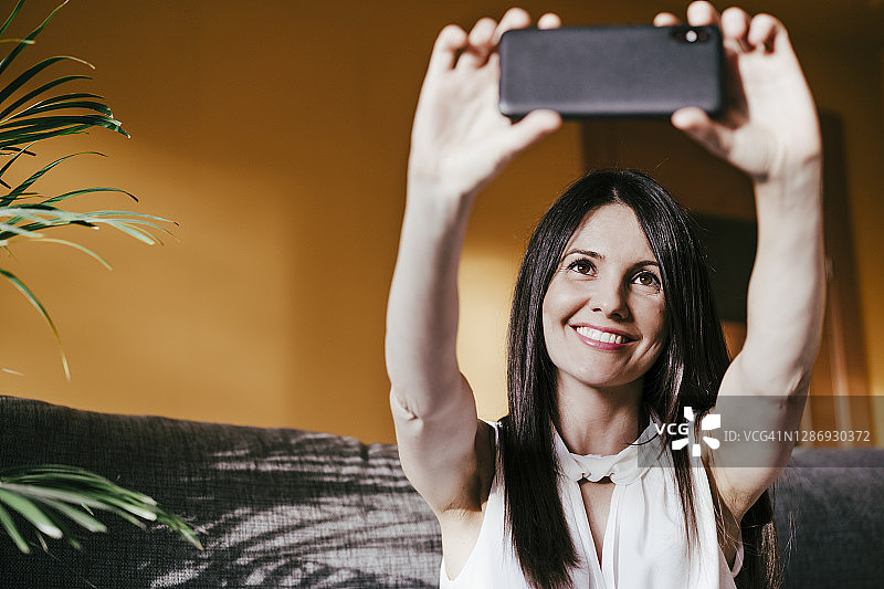 坐在家里用智能手机自拍的微笑女人图片素材