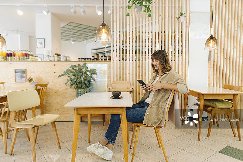 微笑的女商人坐在咖啡馆里用智能手机发短信图片素材