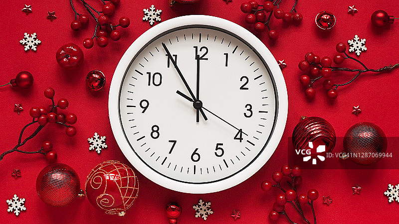 新年和圣诞节旗帜的概念。白色挂钟在节日装饰，红色球，浆果和白色雪花在红色背景，俯视图，平铺。新年和圣诞节之前的时间图片素材