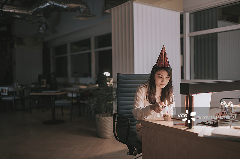 亚裔中国美女独自工作到很晚在办公室庆祝她的生日视频会议与她的同事在其他分行图片素材