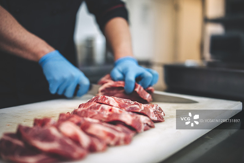 男屠夫在餐厅厨房用锋利的刀切生肉图片素材