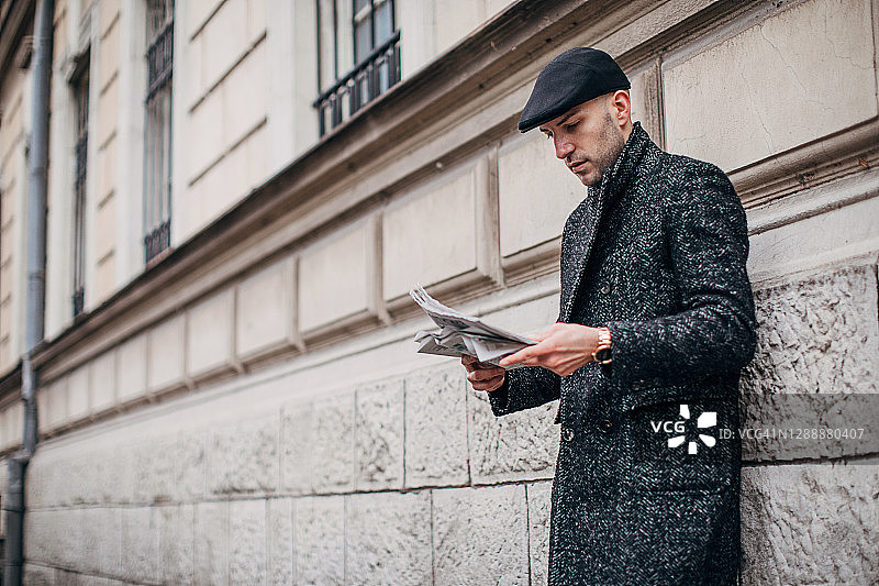 年轻英俊的男子穿着温暖的现代外套在城市的街道上看报纸图片素材