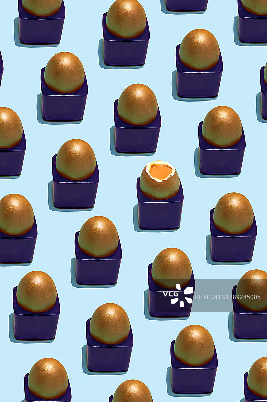 金色的鸡蛋和一个半熟的鸡蛋在蛋杯在蓝色的背景图片素材