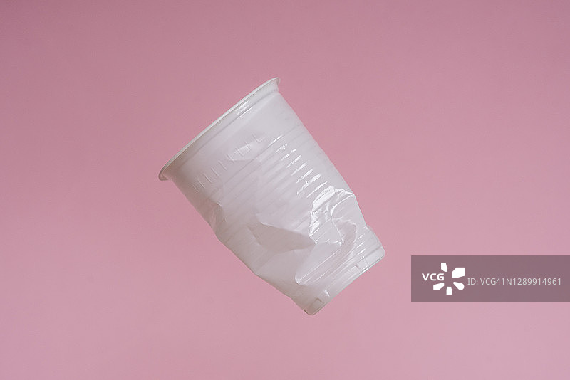 一个一次性塑料杯在粉红色的背景上飞舞。垃圾,塑料盘子图片素材
