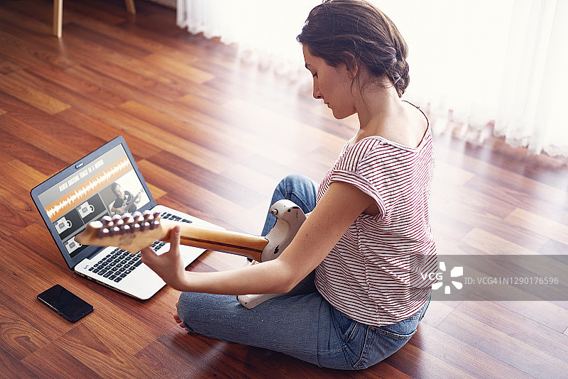 漂亮的年轻女子在笔记本电脑前弹电吉他。音乐学习的概念图片素材