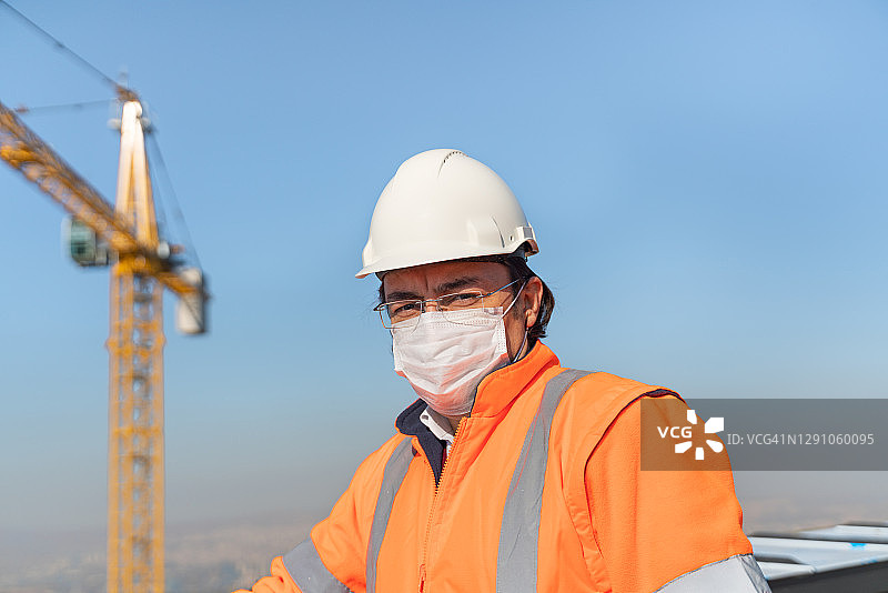 男工程师戴着安全帽和防护面罩在施工屋顶塔吊前微笑图片素材