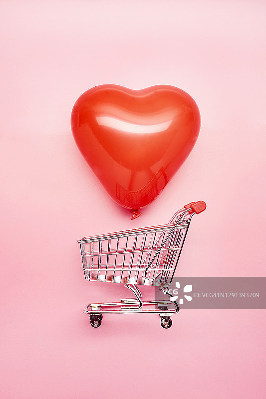 一个小购物车和心形的红色气球在粉红色的背景下的静物，网上购物图片素材