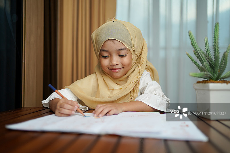 一个穆斯林孩子一边做作业一边看书。孩子喜欢在家里快乐地学习。聪明，教育和聪明的学习理念。图片素材