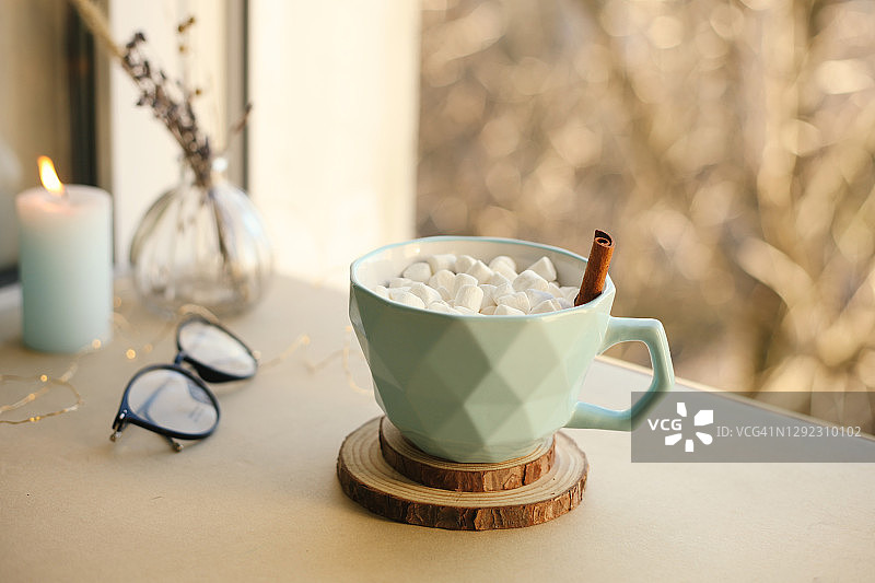 热喝咖啡在蓝色杯与棉花糖和肉桂棒，蜡烛和家庭内部细节窗台，冬季舒适的圣诞图片。图片素材