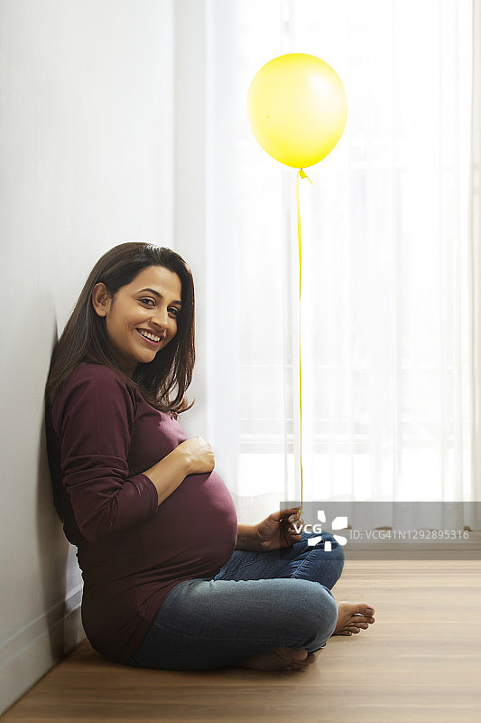 孕妇坐在那里，手里拿着一个黄色的气球，面带微笑。图片素材