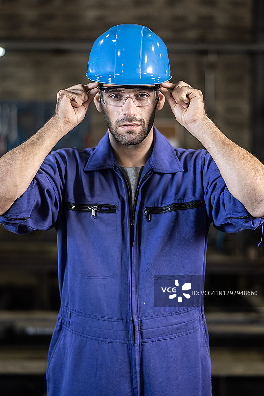 白人工人穿着蓝色工作服和头盔，站在工厂车间里图片素材