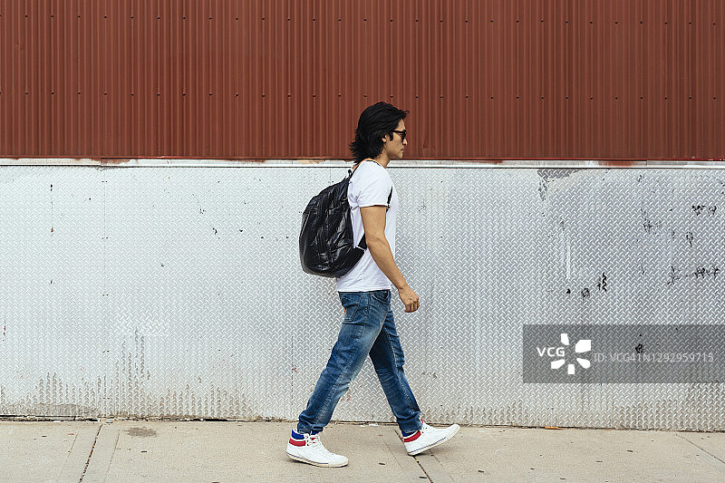 一个背着背包的男人走在人行道上图片素材
