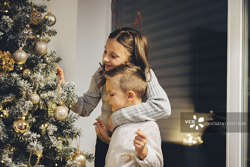 年轻女孩微笑着拥抱她的哥哥站在圣诞树旁图片素材