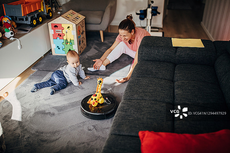 当妈妈和婴儿在地板上玩的时候，机器人真空吸尘器在清洁地板图片素材
