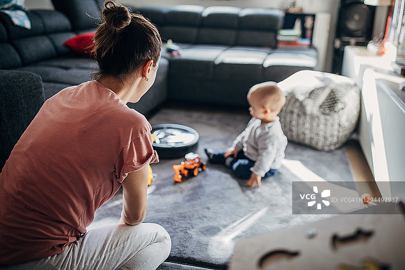 当妈妈和婴儿在地板上玩的时候，机器人真空吸尘器在清洁地板图片素材