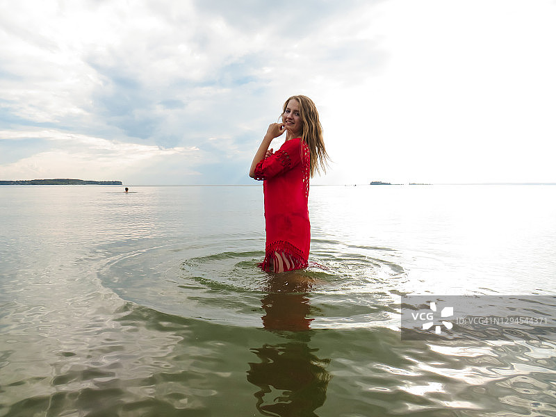 年轻女子与松散的红头发在一个炎热的夏天，红色的海滩连衣裙在海水浅水的海湾图片素材