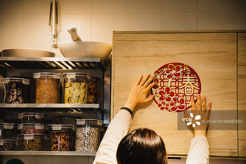 亚洲女性通过在壁柜上贴纸工艺品来庆祝春节图片素材