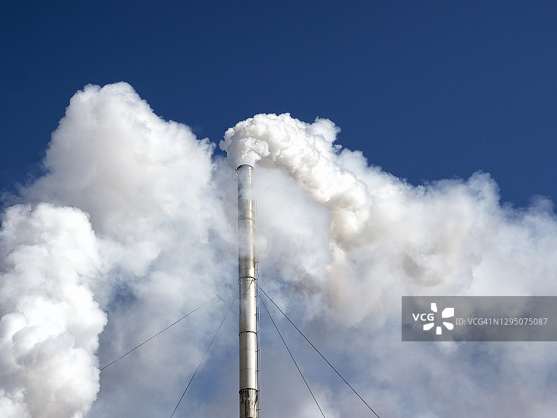 蓝天之上，工业工厂的烟囱向大气中排放烟雾和气体污染。图片素材
