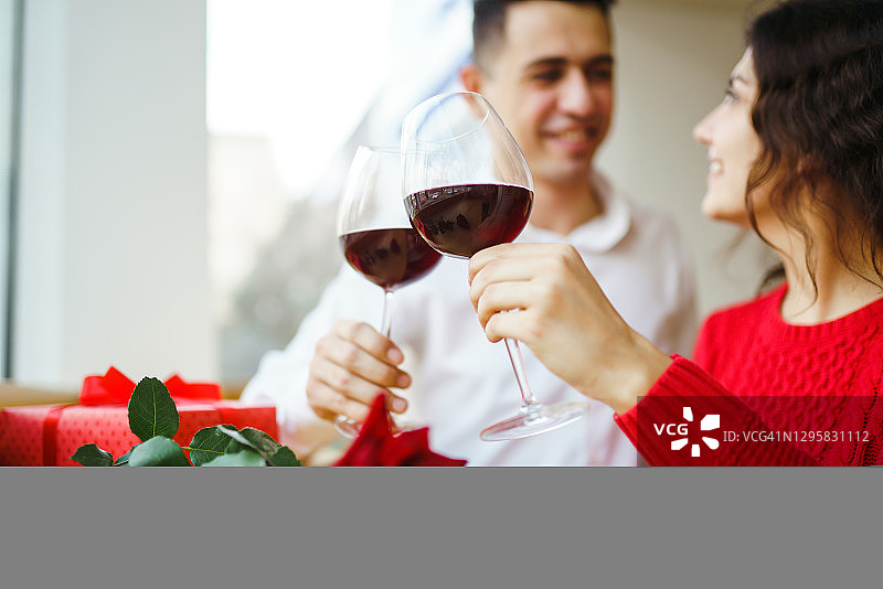 年轻夫妇在享受浪漫的晚餐，并用一杯红酒敬酒。情人节，节日概念。图片素材