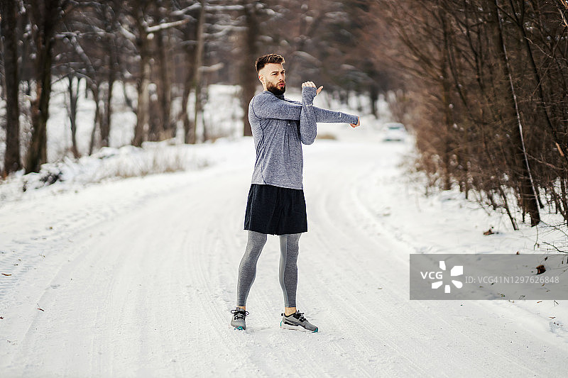 冬天，健硕的运动员站在森林里的雪道上做伸展运动和热身运动。健康生活，冬天健身，寒冷天气图片素材