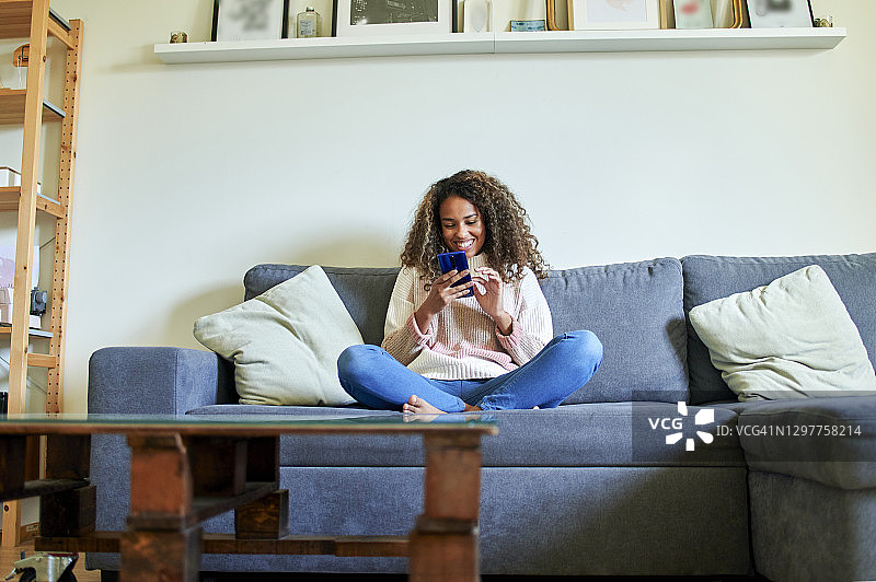 非洲裔年轻女子微笑着在客厅的沙发上使用手机图片素材