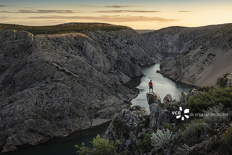 日落时分，一个人站在岩石上，看着峡谷里的河流图片素材