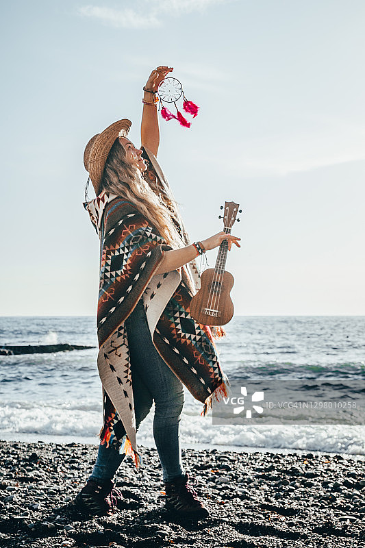 一名女子身穿厄瓜多尔民族斗篷，头戴草帽，在海滩上跳舞。尤克里里琴。轮廓光。图片素材