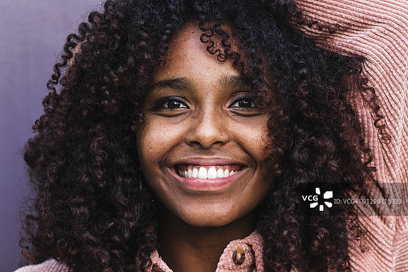 一头卷发靠在墙上的快乐非洲式年轻女子图片素材
