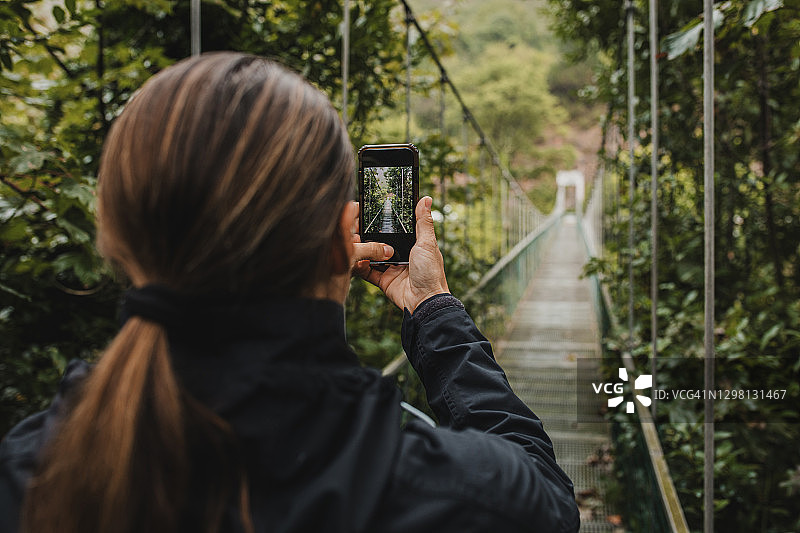 一名女子在森林中的吊桥上用手机拍照图片素材