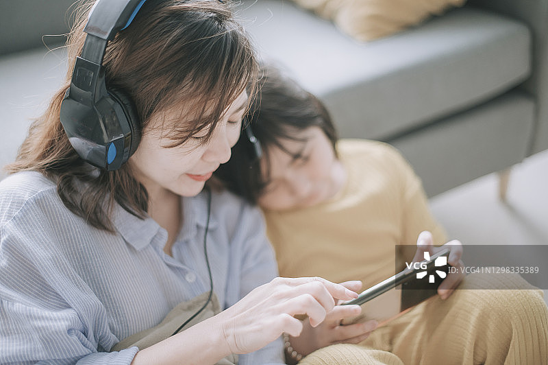 亚洲华人母亲在周末的闲暇时间和女儿在客厅里用耳机听音乐，享受亲子时光图片素材