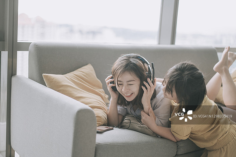 亚洲华人母亲在周末的闲暇时间和女儿在客厅里用耳机听音乐，享受亲子时光图片素材