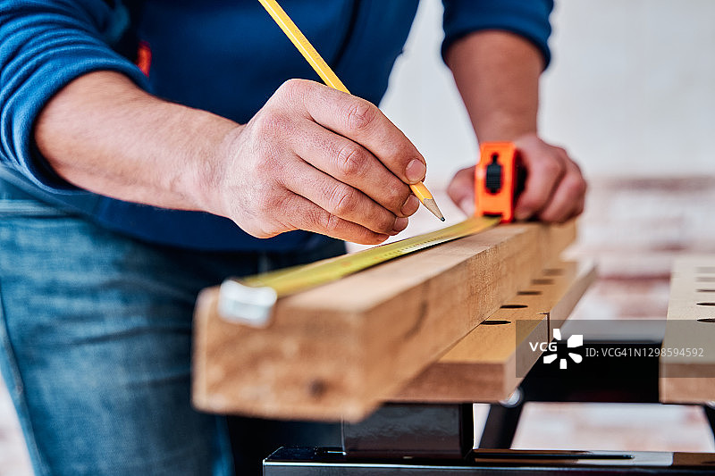 一个男人的手用卷尺在一块木头上测量的细节视图。diy的概念，木工和木工在家里。图片素材