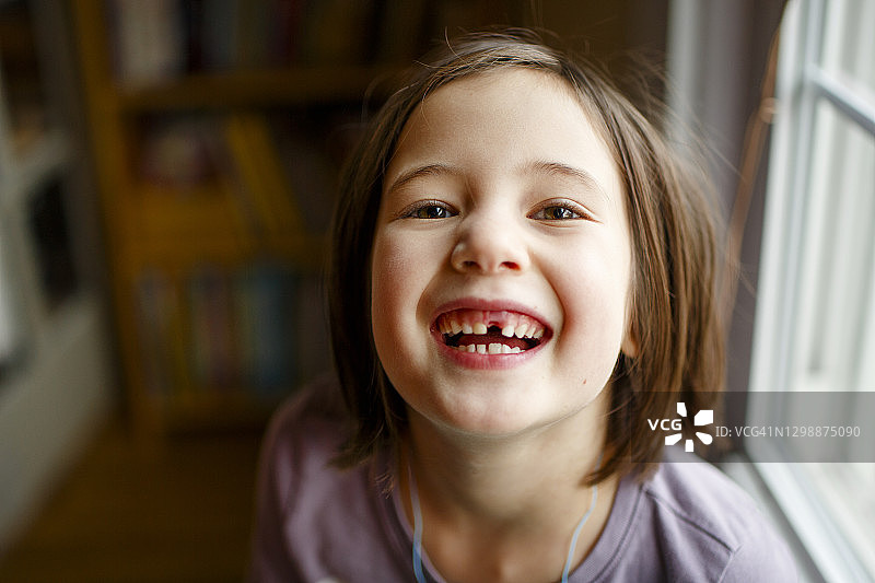 一个有着明亮眼睛的可爱女孩骄傲地展示着一颗缺失的牙齿图片素材