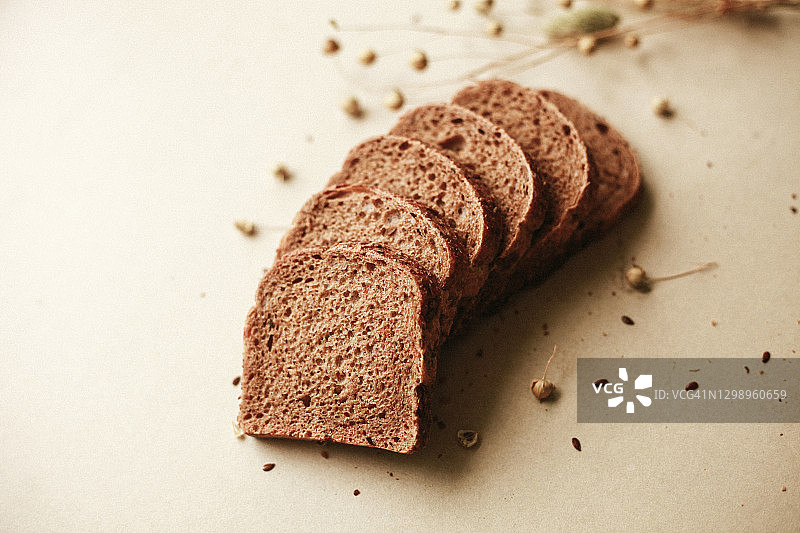 切片的黑色面包和亚麻籽和作物在米色自然背景图片素材